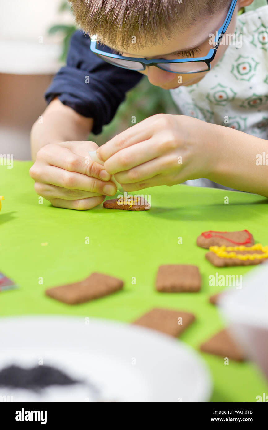 Ein Kind in der Küche. Cookies mit bunter Zuckerglasur verzieren. Die Hände des Kindes drücken Sie die Glasur in Gelb. Stockfoto