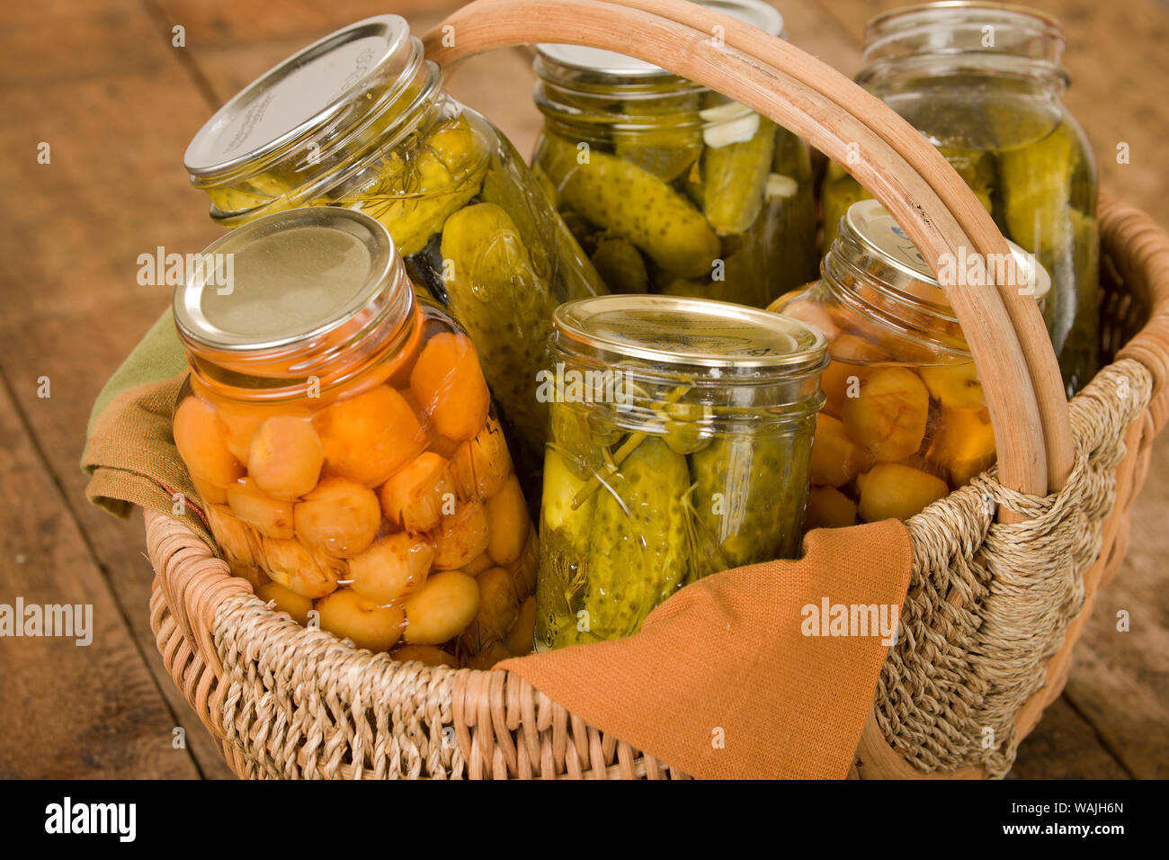 Heimat-dosen produzieren (Rainier Kirschen und Dill Pickles) in einem großen Weidenkorb ruht auf einem rustikalen hölzernen Tischplatte. Stockfoto