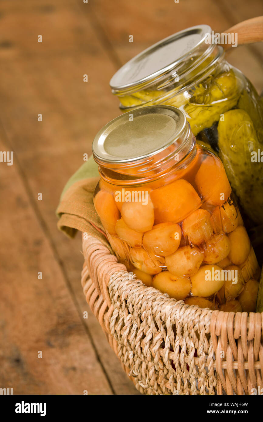 Heimat-dosen produzieren (Rainier Kirschen und Dill Pickles) in einem großen Weidenkorb ruht auf einem rustikalen hölzernen Tischplatte. Stockfoto