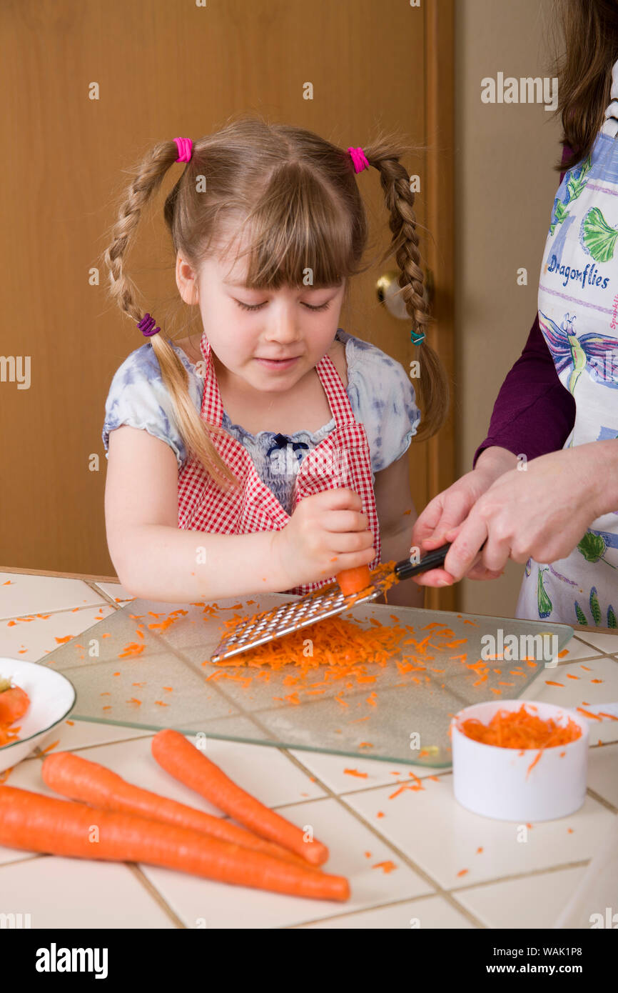 Mädchen Gitter Karotten, unterstützt von ihrer Mutter, für einen Karottenkuchen. (MR, PR) Stockfoto