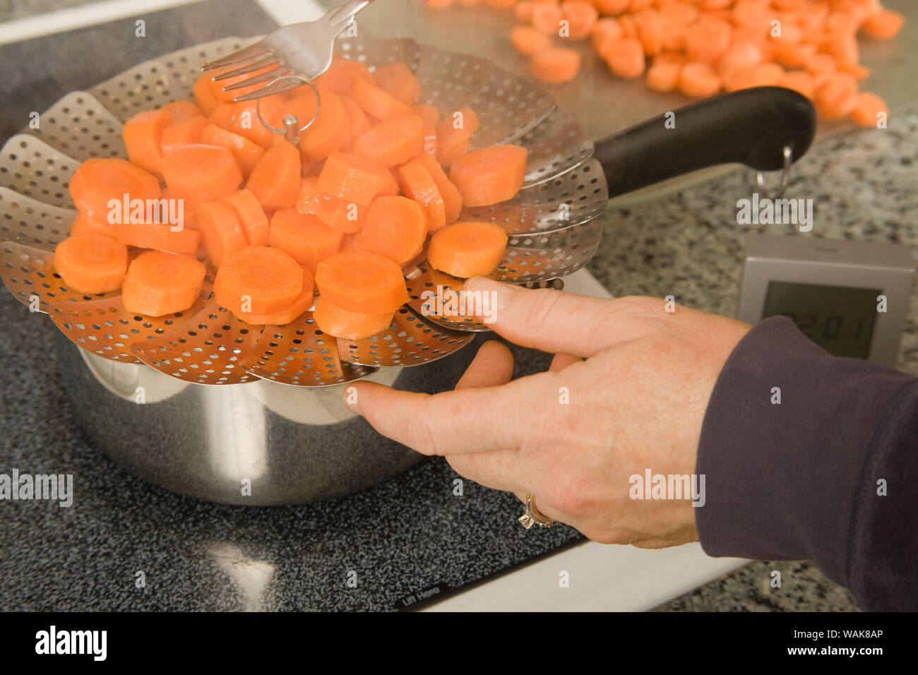 Frau ziehen erweiterbar Sieb aus Topf wo Karotten in Vorbereitung für das Einfrieren blanchiert wurden. (MR) Stockfoto