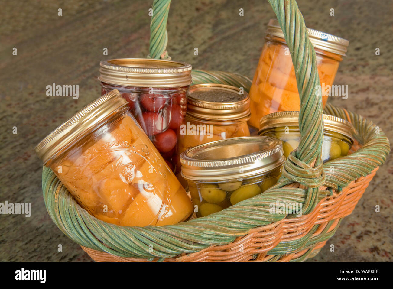 Weidenkorb von zu Hause Konserven (Pfirsiche, Oliven und Kirschen) auf einem Granit Arbeitsplatte in der Küche. Stockfoto