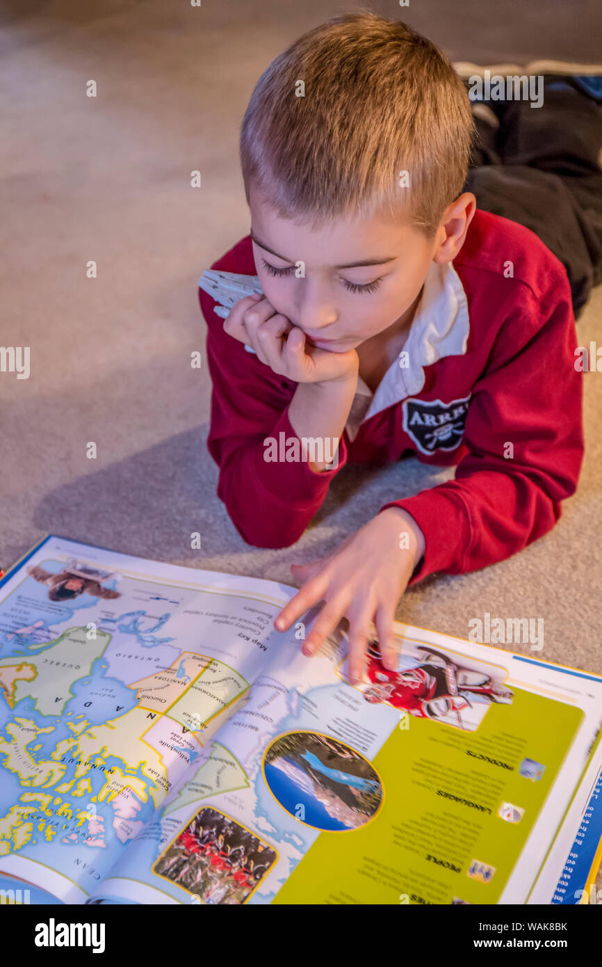 Sieben Jahre alten Jungen lesen seine Welt Atlas Buch. (MR) Stockfoto