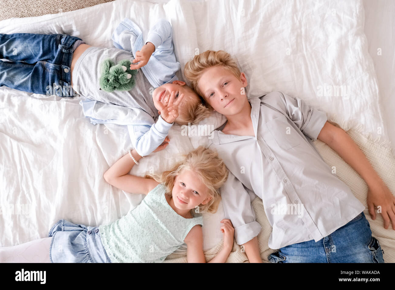 Drei fröhliche blonde Kinder sind zusammen auf dem Bett liegend, mit