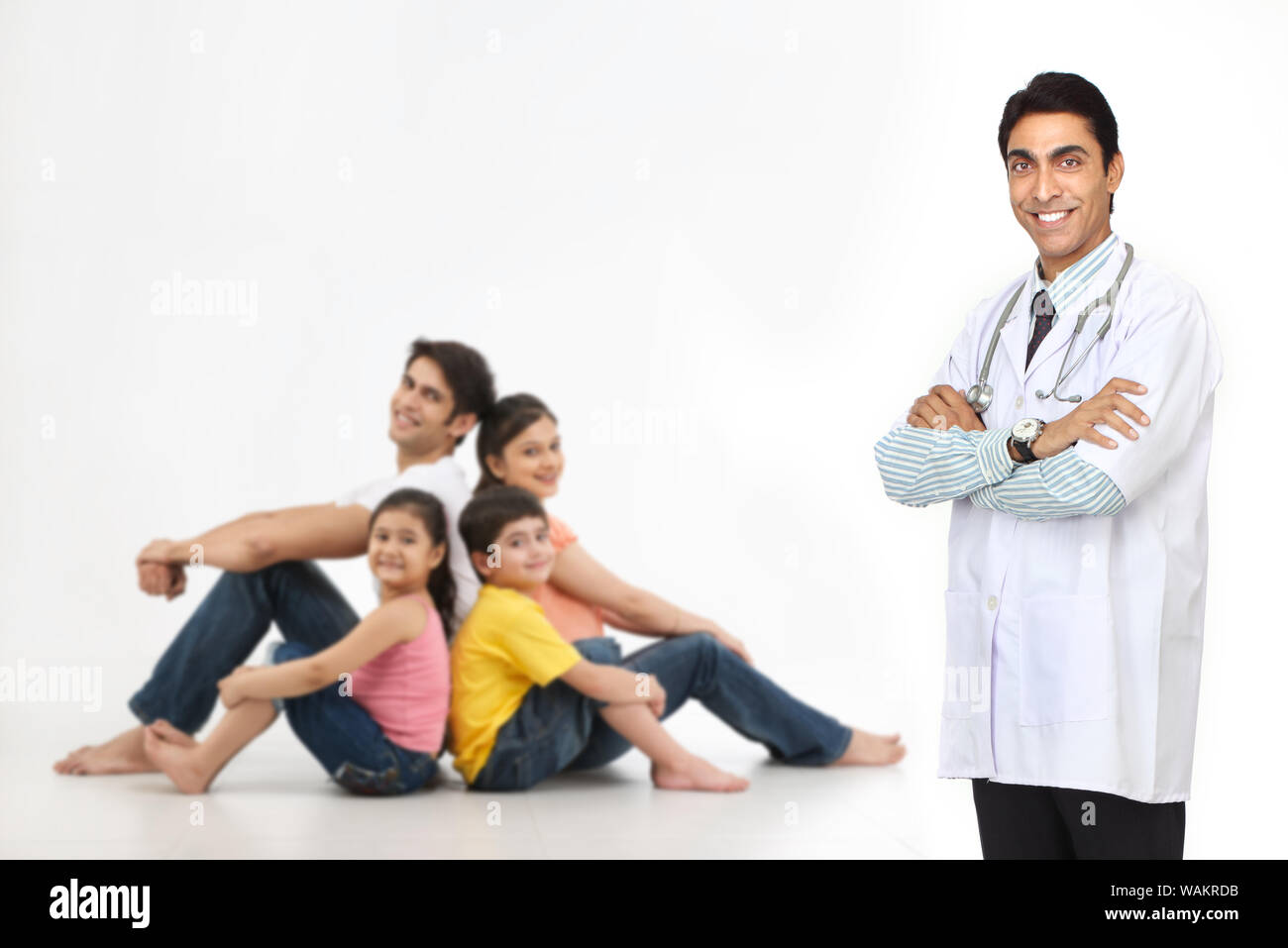 Doktor steht mit gekreuzten Armen und Familie sitzt im Hintergrund Stockfoto