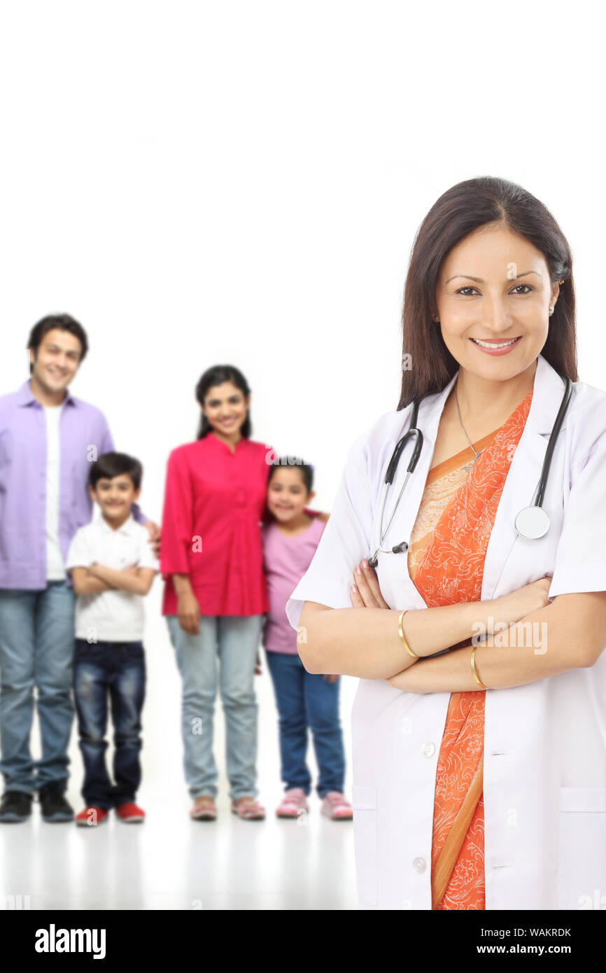 Doktor steht mit gekreuzten Armen und Familie im Hintergrund Stockfoto