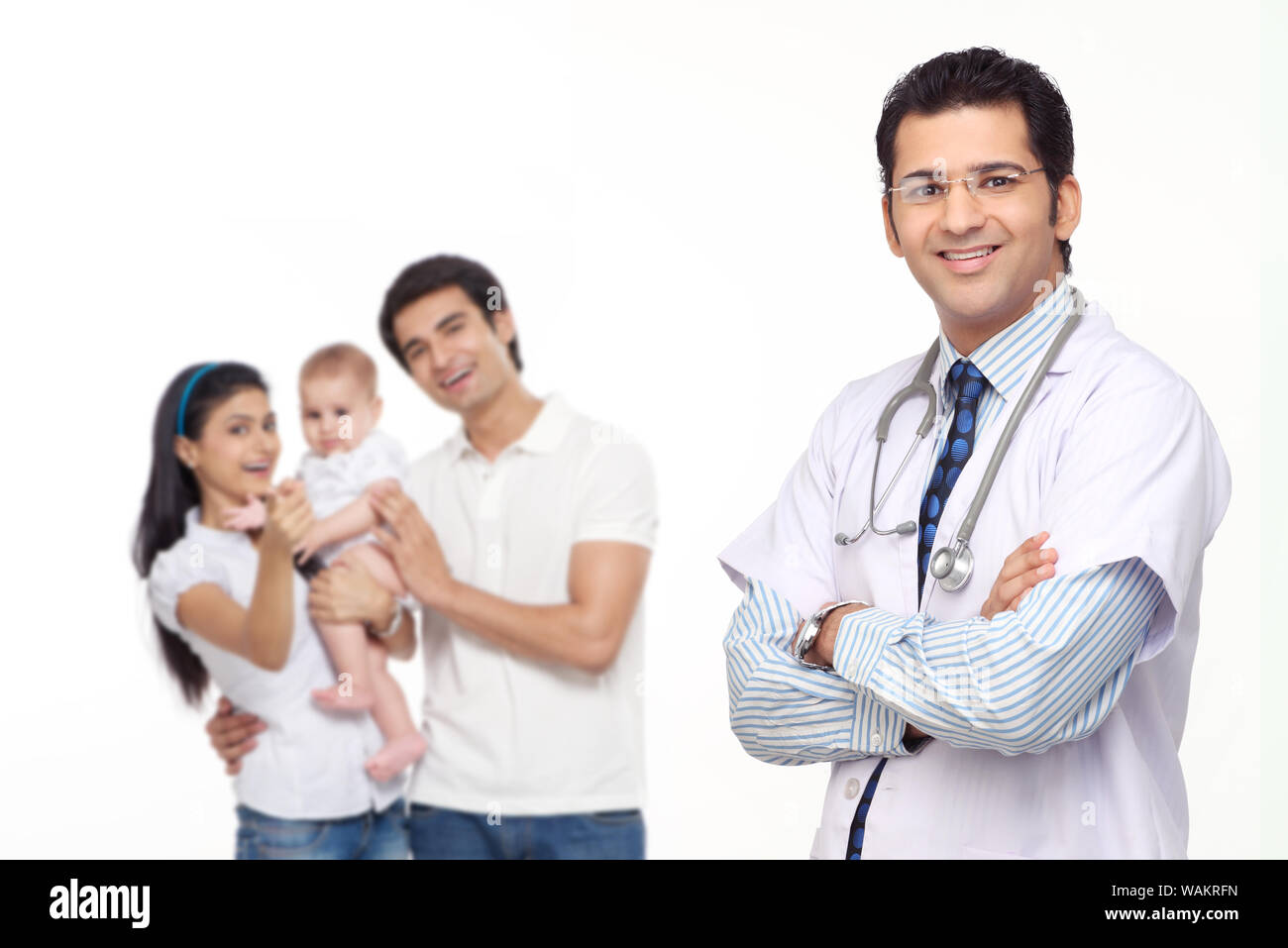 Doktor steht mit gekreuzten Armen und Familie steht im Hintergrund Stockfoto