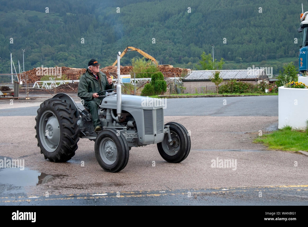 Man Grüne wasserdichten Anzug Fahren 1956 Vintage Grau Grey Fergie Massey Ferguson Traktor männlichen vorne abseits Treiber Seitenansicht Veteran glänzenden heiligen Loc Stockfoto