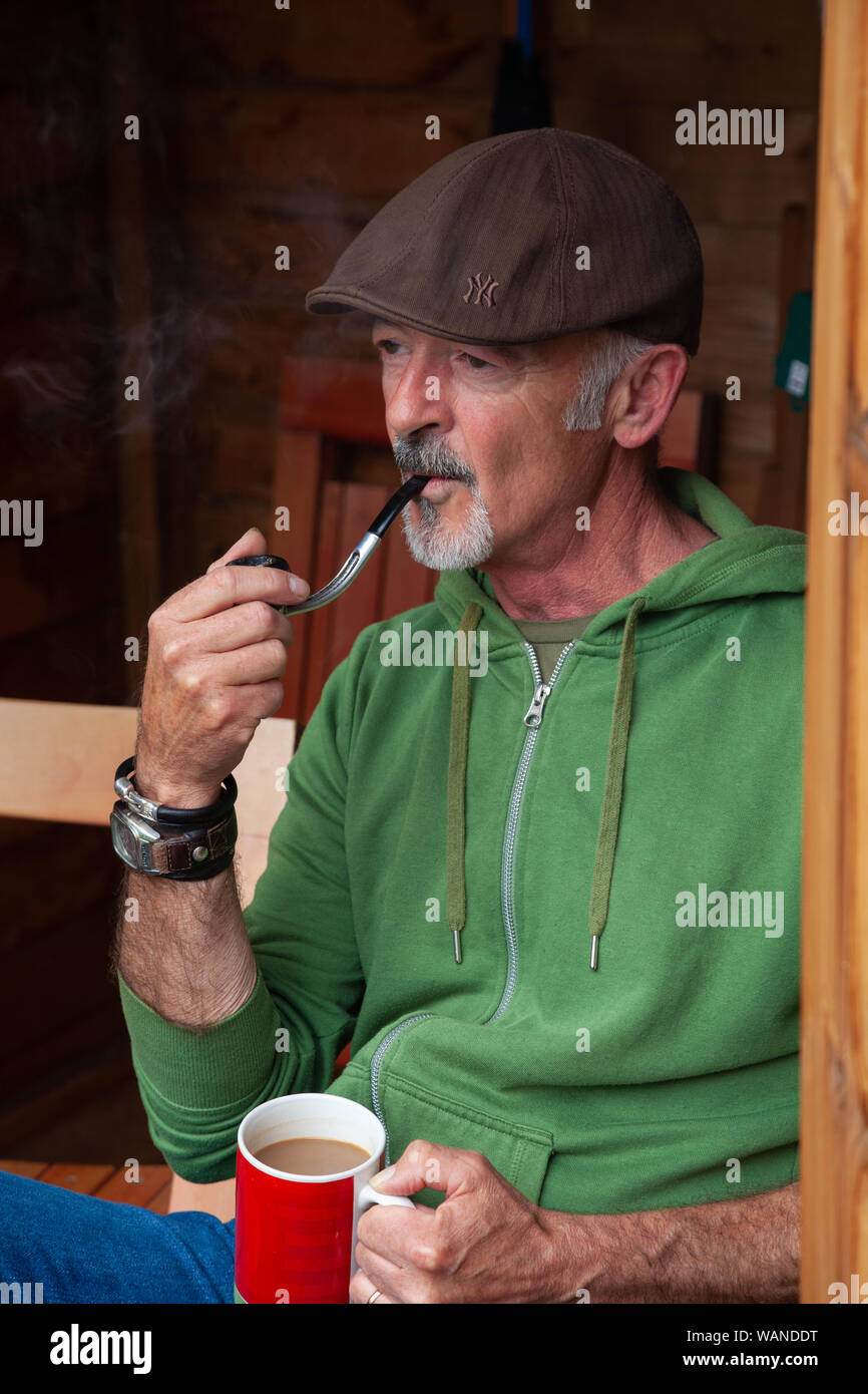 Ein Mann mittleren Alters saß in einem Schuppen und Rauchen ein Rohr. Stockfoto