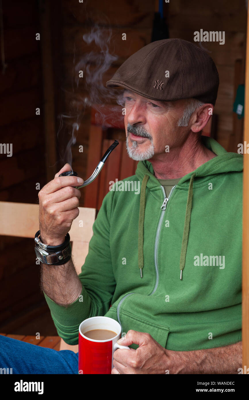Ein Mann mittleren Alters saß in einem Schuppen und Rauchen ein Rohr. Stockfoto