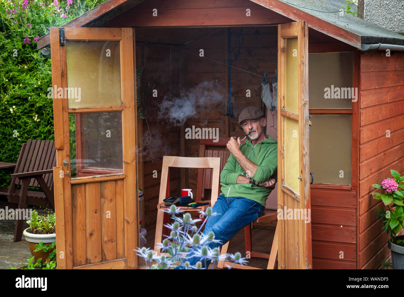 Ein alter Mann sitzt in einem Gartenhaus und Rauchen ein Rohr. Stockfoto