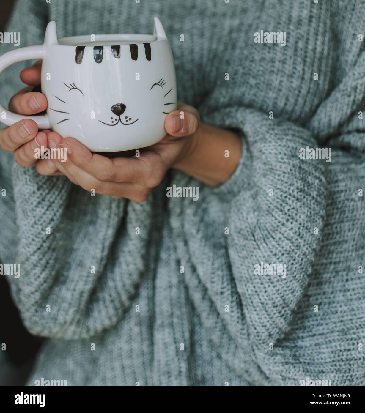 Aufnahme einer Frau trägt blauen Pullover mit einem niedlichen Weißer Becher mit dem Gesicht eines glücklichen Kätzchens Stockfoto