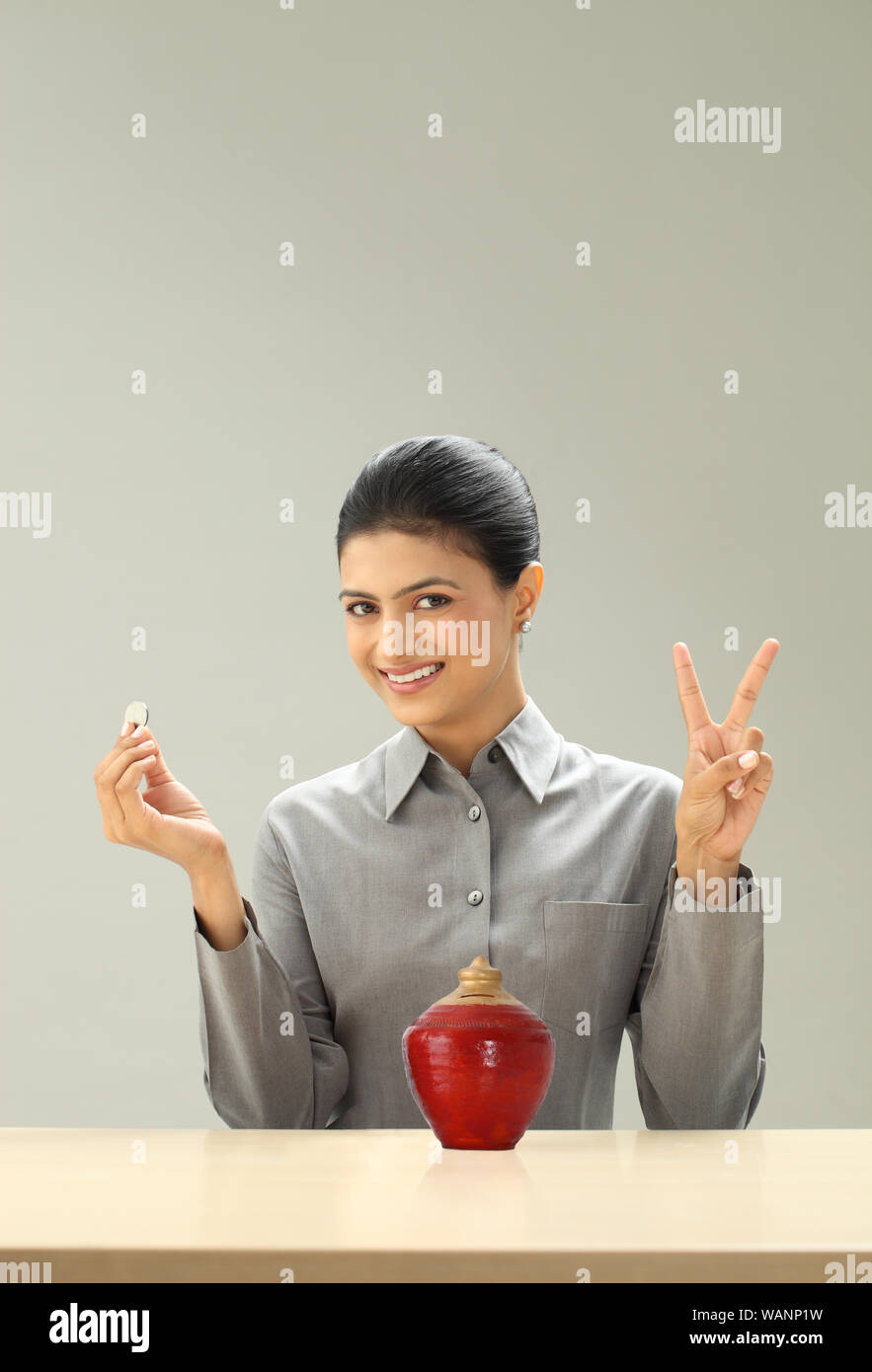 Geschäftsfrau zeigt V-Zeichen und hält Münze Stockfoto