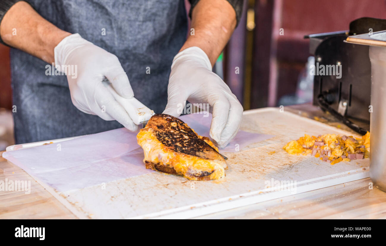Chef an einer Straße Markt vorbereiten Sandwich mit gegrilltem geschmolzenem Käse und Speck Stockfoto