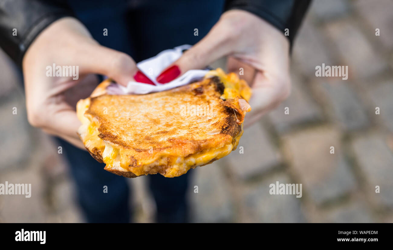 Essen ein Sandwich mit gegrilltem geschmolzenem Käse und Speck zu einem Street Food Markt Stockfoto