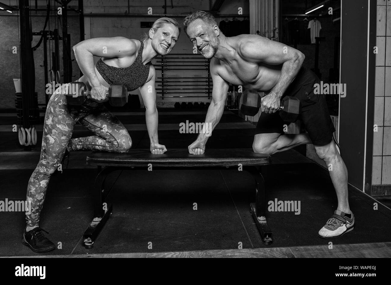 Einen mittleren Alters attraktiv und sportlich Paar ist eine funktionelle Fitness Training mit Kurzhanteln. Mann und Frau sind das Lachen in der Turnhalle. Stockfoto