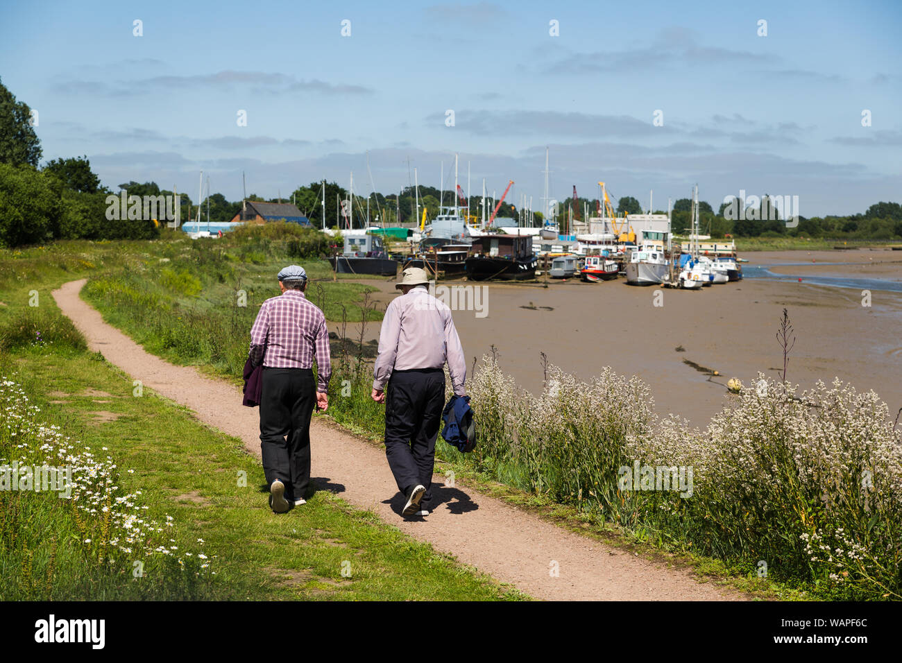 2 pensionierte Männer, einen Spaziergang in der Sonne entlang eines Flusses mit Booten in den Hintergrund, die River Deben Suffolk Stockfoto