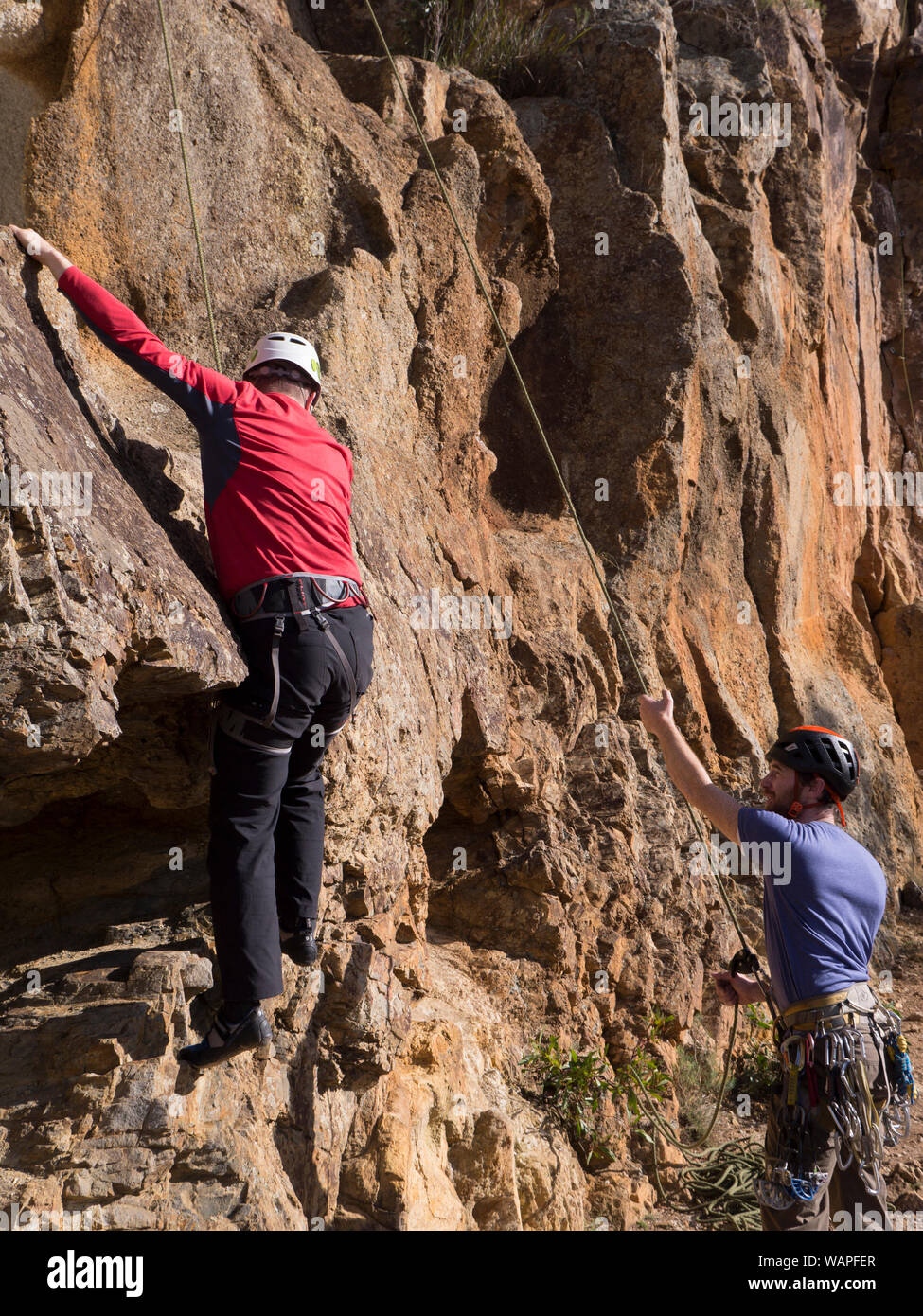 Technische klettern Instructor, sichern einen unerfahrenen Bergsteiger und Kletterer zeigen Angst, nervöse, wo Hände und Füße auf die Felswand in Australien. Stockfoto