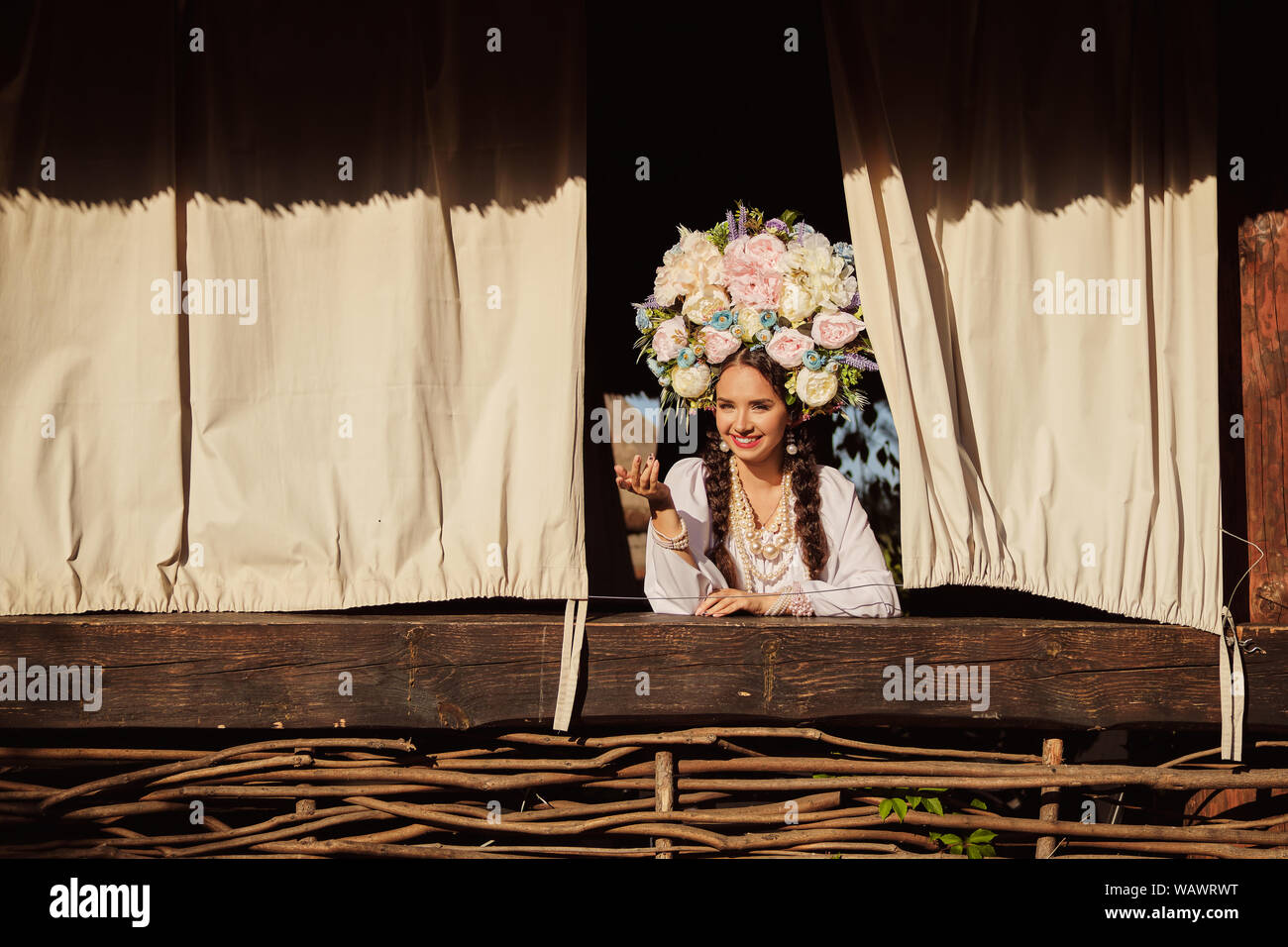 Brünette Mädchen in einem weißen ukrainischen authentische nationale Kostüm und ein Kranz aus Blumen ist schaut aus dem Fenster. Stockfoto