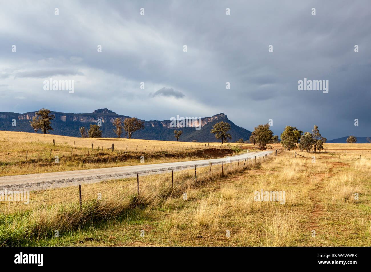 Leere Landstraße durch Bergwiesen in der capertee Valley, NSW, Australien schneiden, mit Sandstein Bergrücken und natürlichen Buschland im Hintergrund Stockfoto