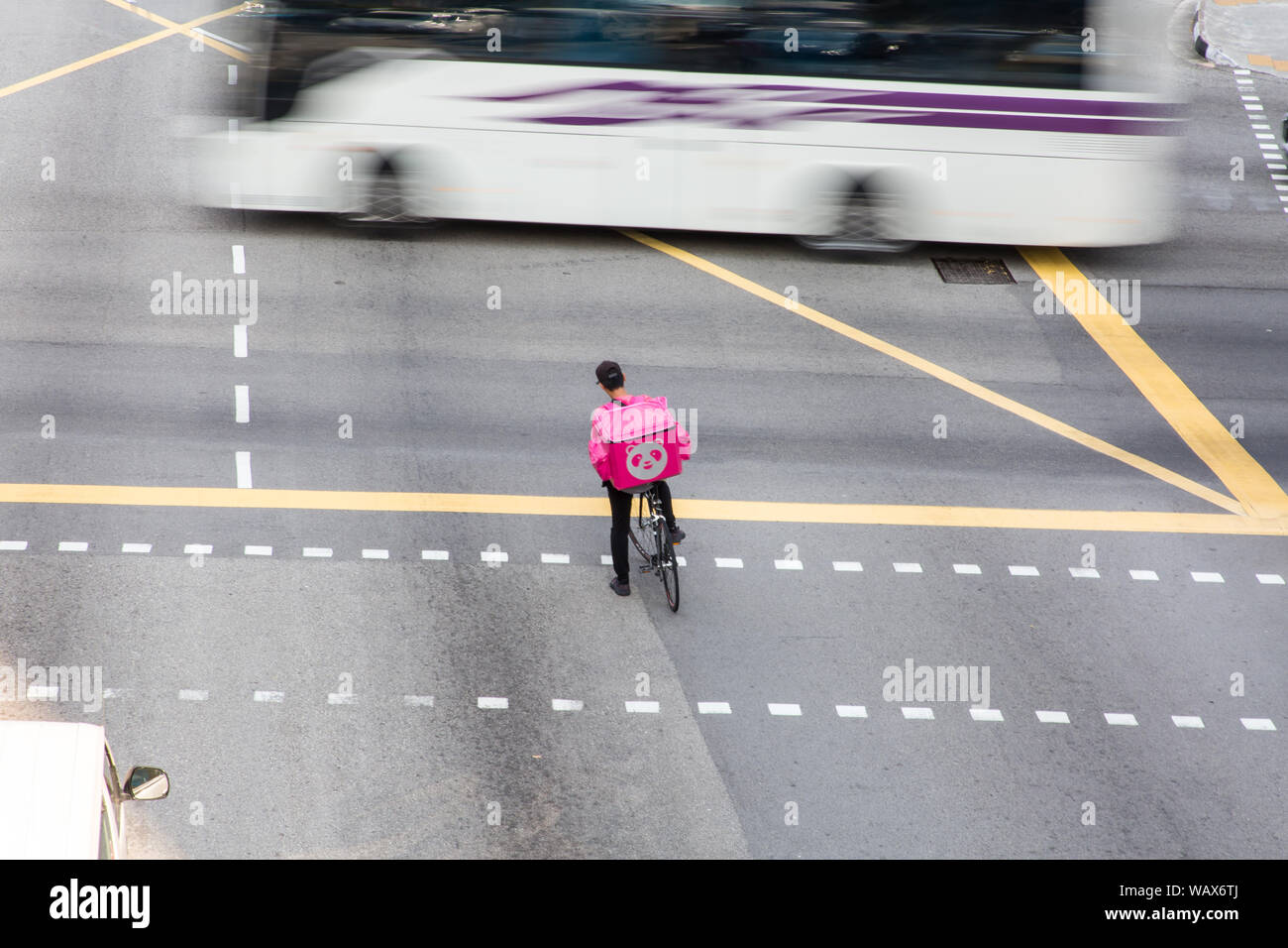 Food Panda Lieferservice Mann mit Kappe, mit seinem Fahrrad auf der Straße, während auf den geschäftigen Verkehr an der Kreuzung warten. Stockfoto