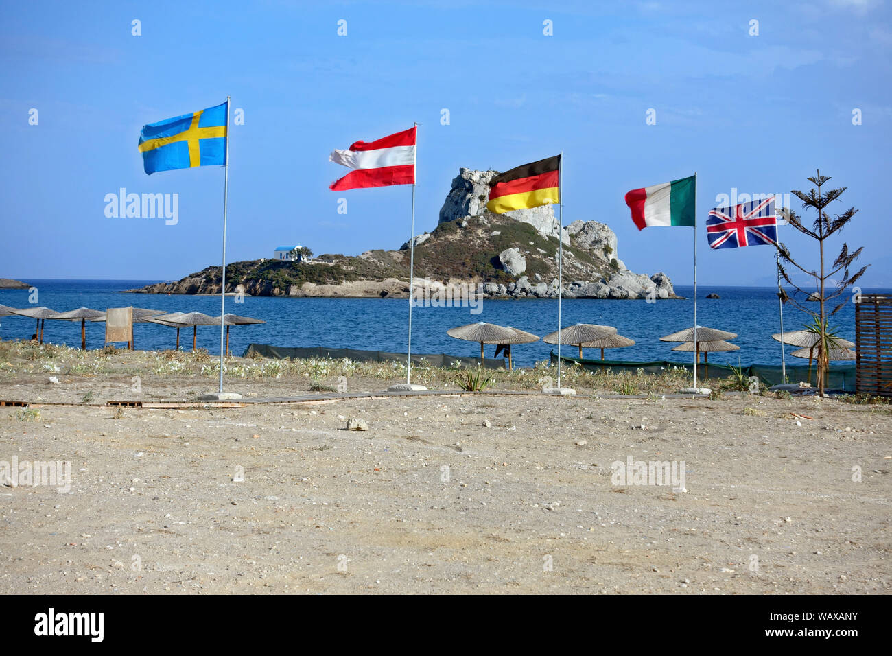 Kos: Fahnen Fliegen am Strand von Agios Stefanos mit Kastri Insel im Hintergrund Stockfoto