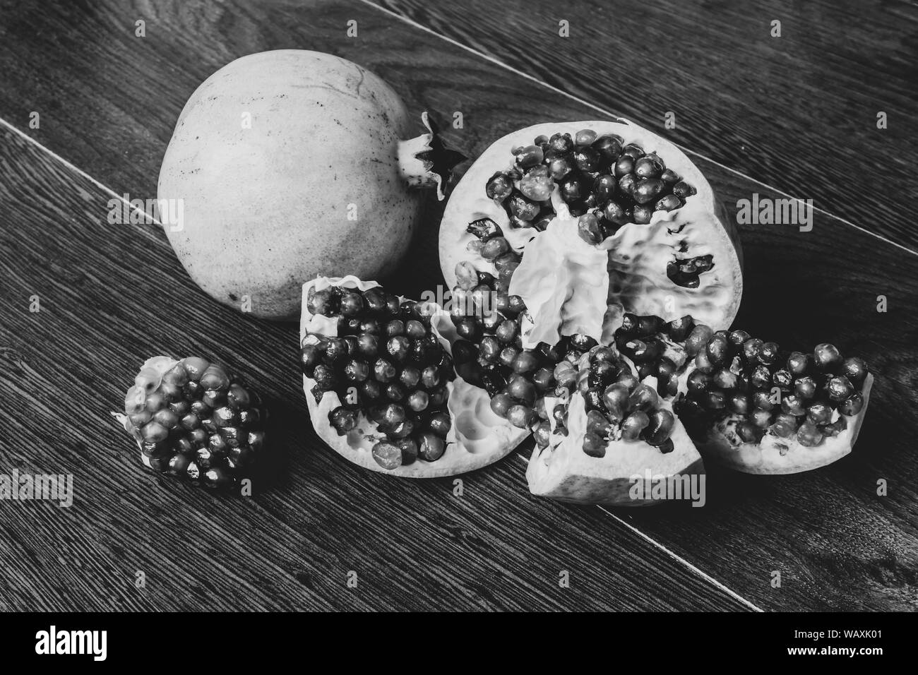 Monochrome Stillleben - ganze und schneiden Granatapfel Obst auf einem dunklen, hölzernen Tischplatte Stockfoto