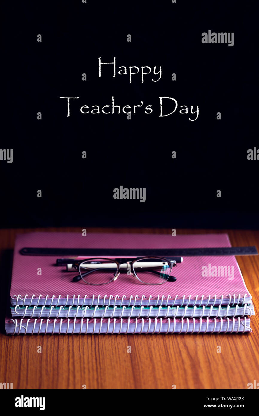 Happy Teachers' Day auf einer Tafel mit einem von Büchern oder Zuordnungen, Gläser, Stifte und Lineal auf einen hölzernen Tisch Stapel geschrieben. Kopieren Sie Platz. Stockfoto