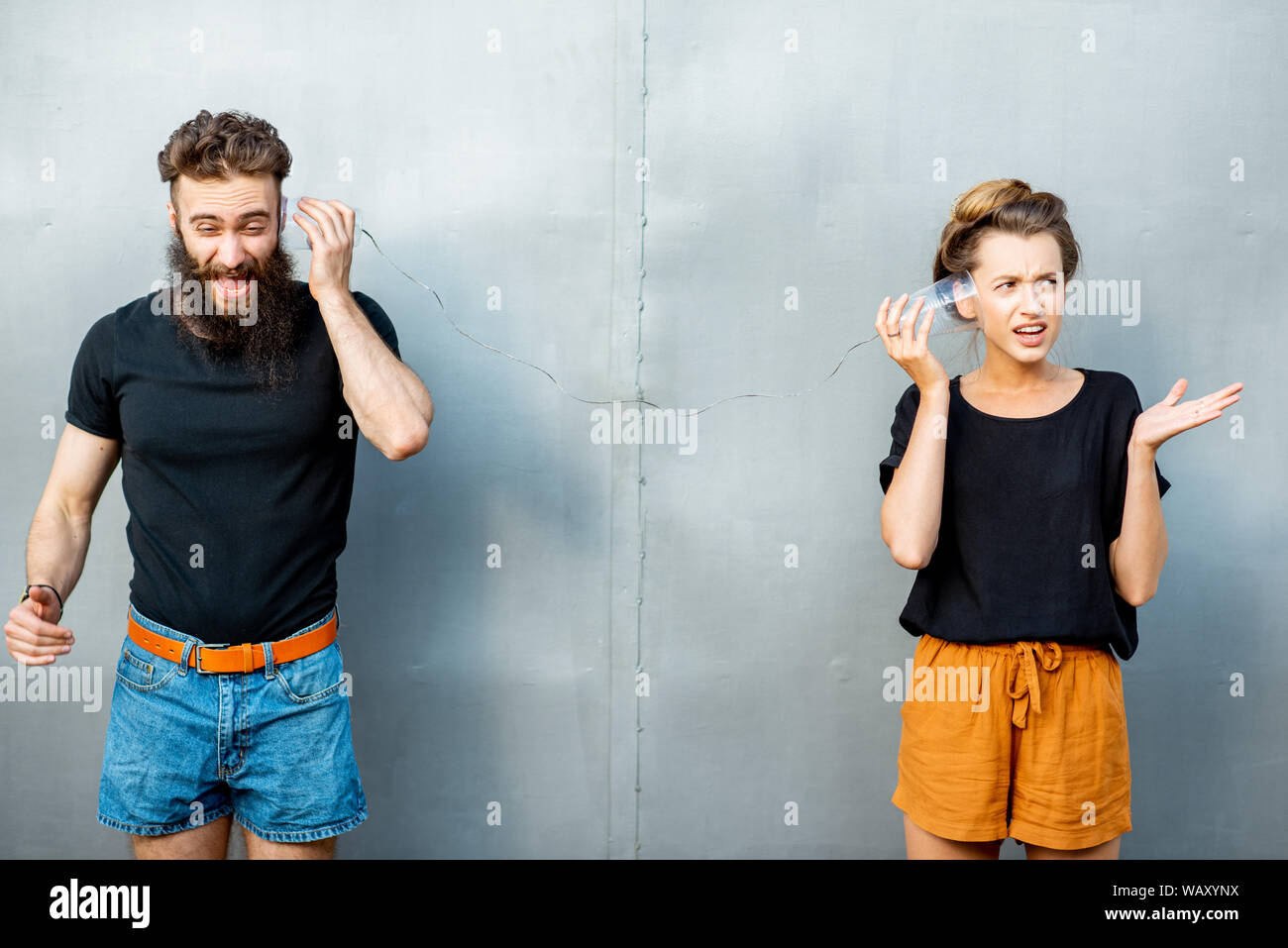 Mann und Frau im Gespräch mit Zeichenkette Telefon von Cups auf dem grauen Hintergrund. Konzept der Kommunikation Stockfoto