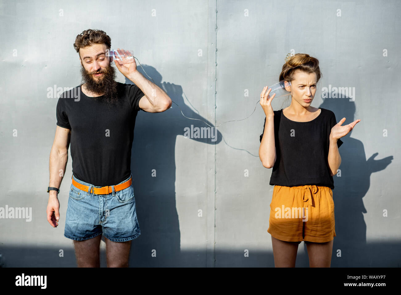 Mann und Frau im Gespräch mit Zeichenkette Telefon von Cups auf dem grauen Hintergrund. Konzept der Kommunikation Stockfoto