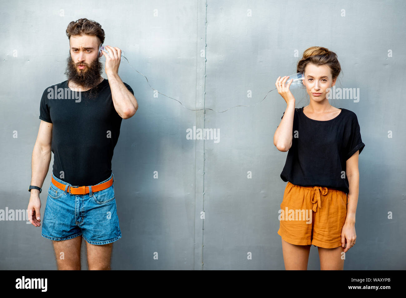 Mann und Frau im Gespräch mit Zeichenkette Telefon von Cups auf dem grauen Hintergrund. Konzept der Kommunikation Stockfoto