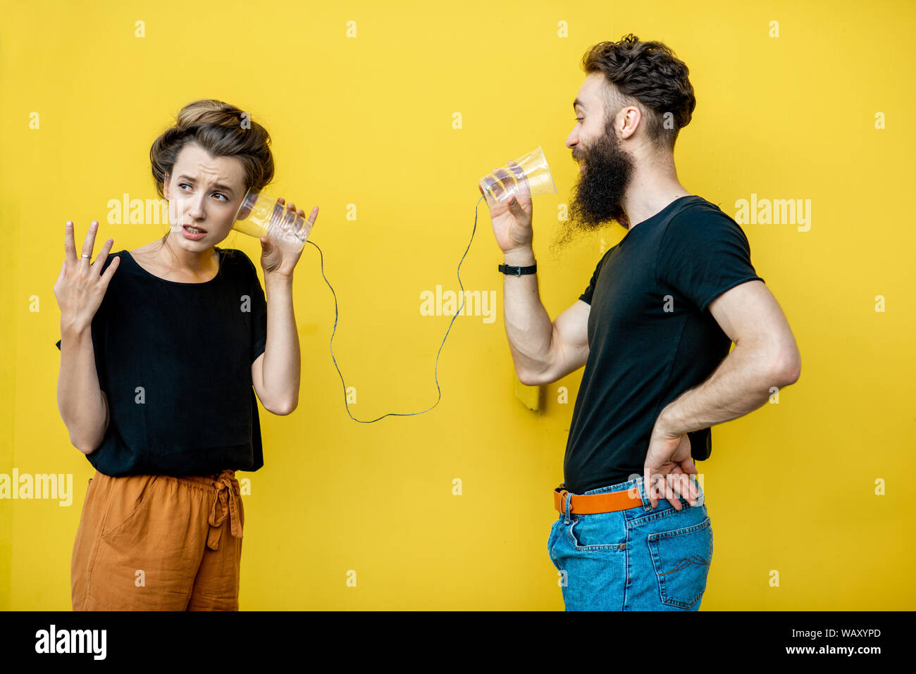 Mann und Frau im Gespräch mit Zeichenkette Telefon von cups auf den gelben Hintergrund. Konzept der Kommunikation Stockfoto