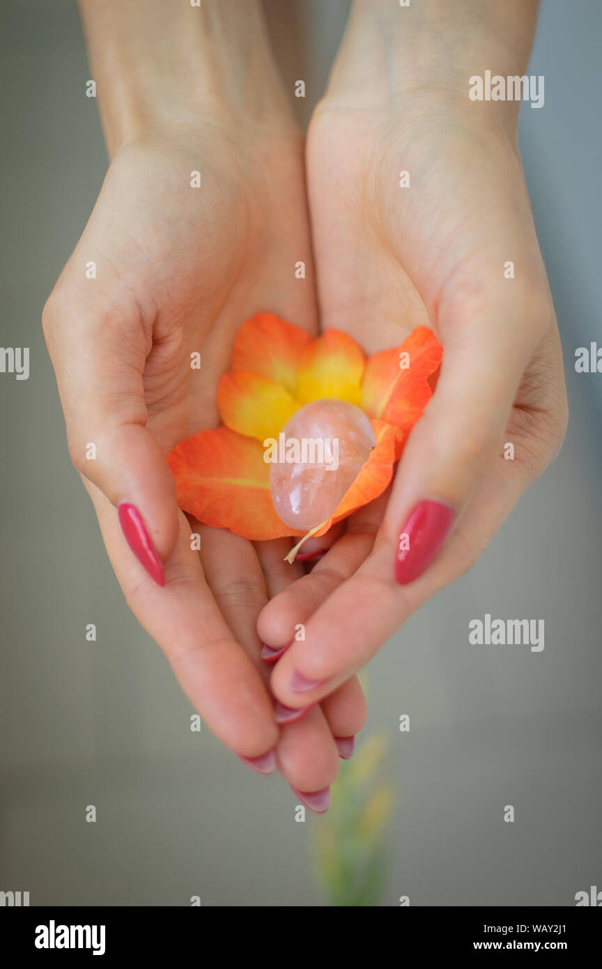 Weibliche hand mit roten Maniküre Holding transparent violett Amethyst yoni Ei für vumfit, imbuilding oder Meditation in Orange und Gelb gladiolus Stockfoto