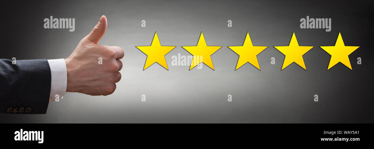 Nahaufnahme der Geschäftsmann mit Daumen hoch, mit Gelb fünf Sterne auf grauem Hintergrund Stockfoto