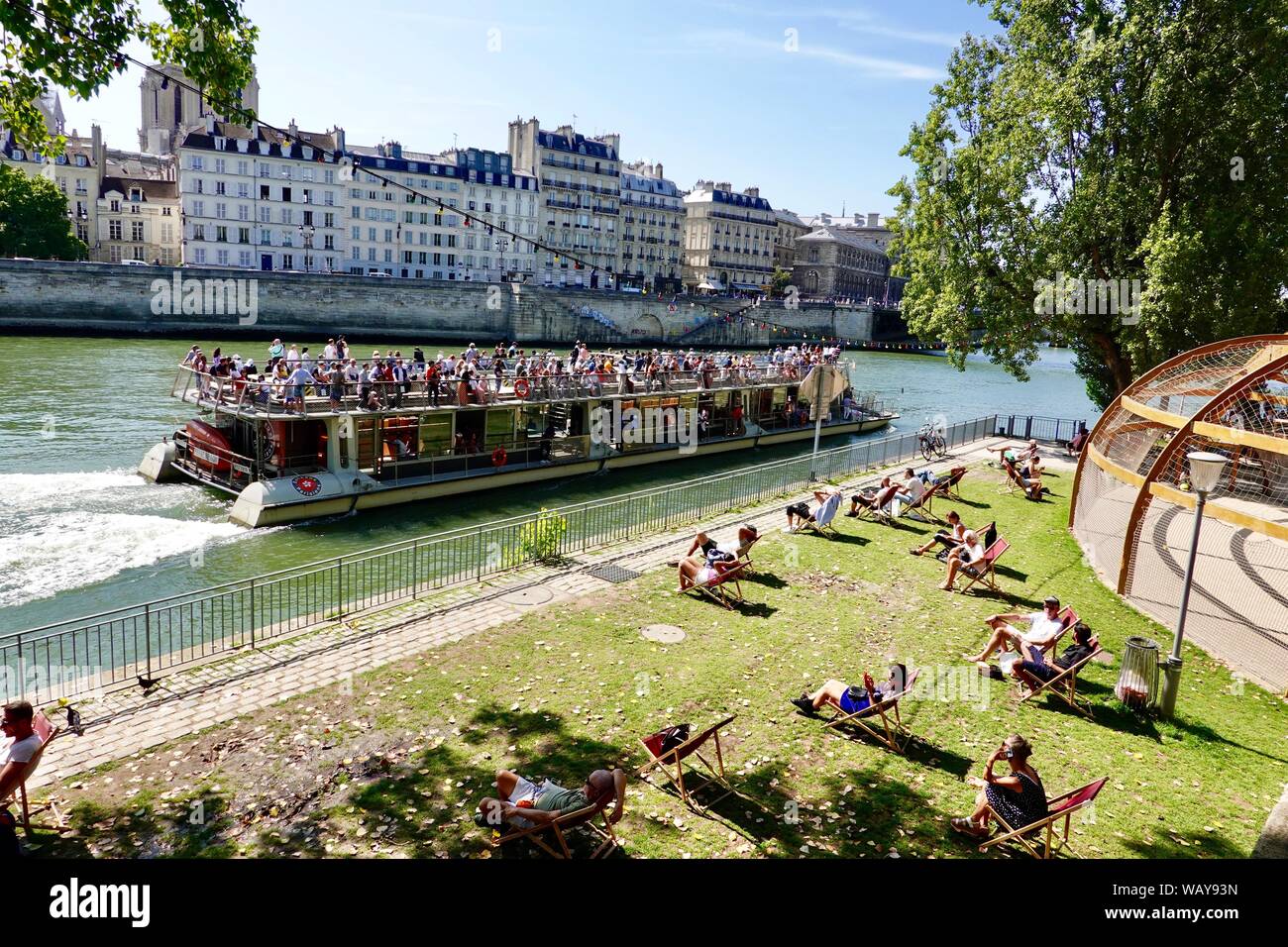 Menschen entspannen im Paris Plage Gebiet entlang der Seine während der warmen Tage im August, als tourist boat Vergangenheit Kreuzfahrten, Paris, Frankreich. Stockfoto