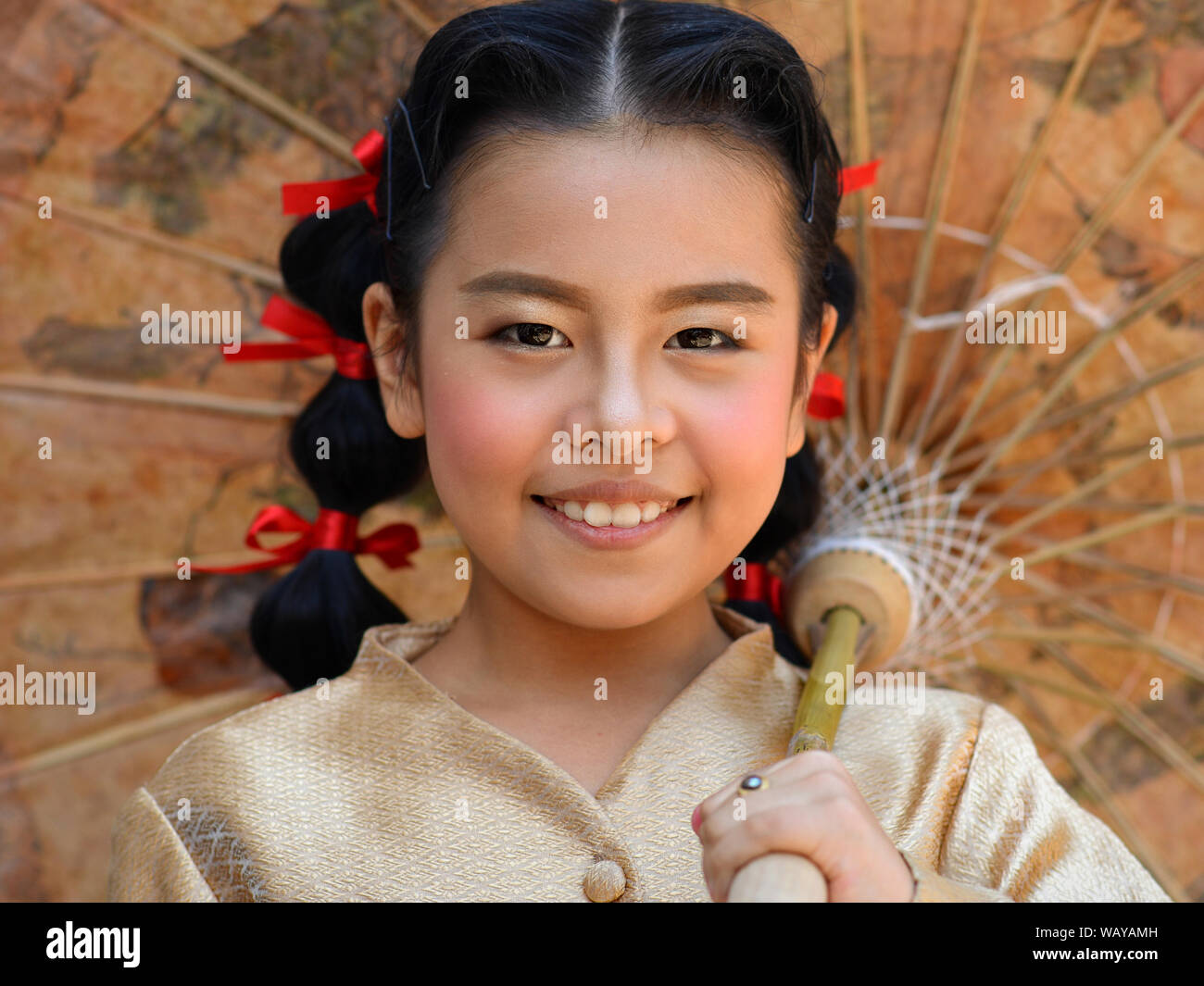 Kostümierte Thai vor - jugendlich Mädchen mit roten Haaren Bänder posiert für die Kamera unter einer traditionellen chinesischen Öl- papier Sonnenschirm. Stockfoto