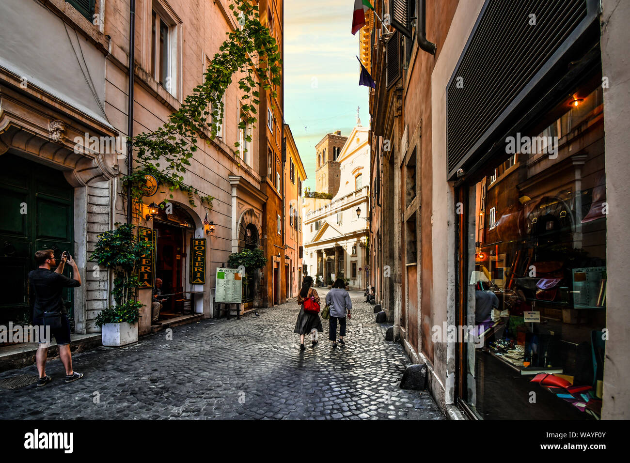 Touristen vorbei an Geschäften, einem schattigen Gasse in Richtung Saint Eustace Kirche mit dem Weißen Hirsch Skulptur auf dem Dach in Rom, Italien Stockfoto