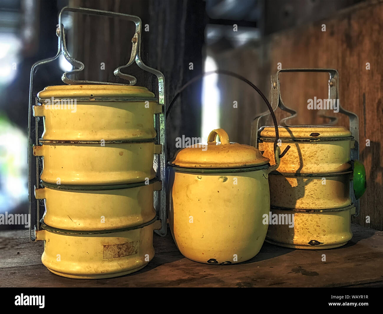 Inszenierte Lunch Box, häufig in asiatischen Ländern verwendet. Alt und rustikal Tiffin Luftfahrtunternehmen und eine gelbe Topf, mit geringer Tiefenschärfe. Stockfoto