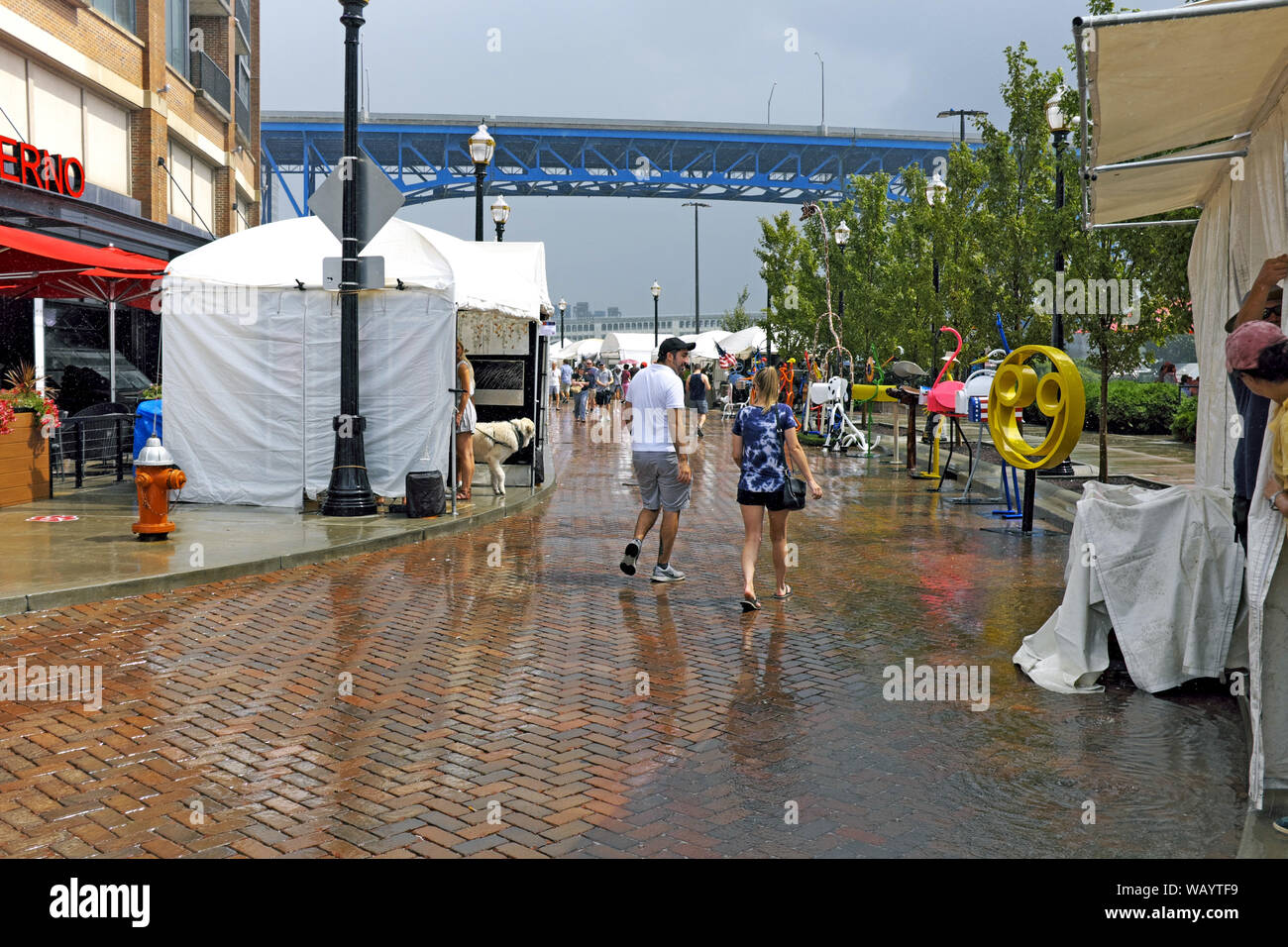 Ein Paar spaziert nach einem Sommerregen entlang der Strandpromenade von Flats East Bank während des 2019 Flats Festival of the Arts in Cleveland, Ohio, USA. Stockfoto