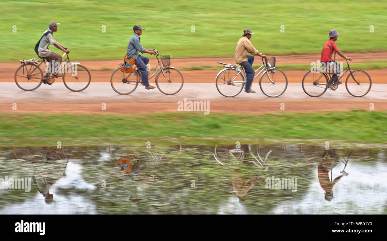 Eine Gruppe von vier Personen, Fahrrad oder Radfahren und die Reflexion auf dem Wasser, während Sie durch die Straßen mit Gras und Pfade Stockfoto