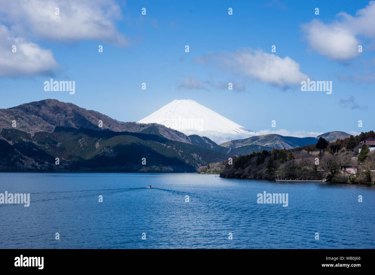 Mount Fuji in Japan bedeckt von Schnee über einen großen See gesehen. Kleines Boot verlassen ein Dreieck bilden, Weckservice, als wenn die Spiegelung der Form des Fuji. Blue Sky Stockfoto