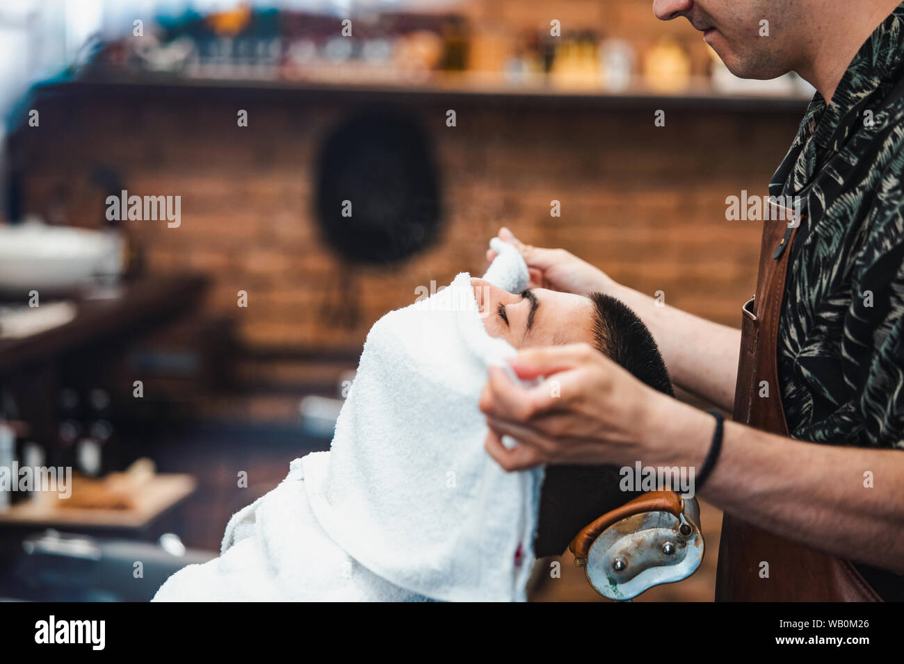Friseur deckt das Gesicht eines Mannes mit einem warmen Handtuch. Traditionelle Ritual der Rasur des Bartes heiße und kalte Kompressen in einem alten Stil Friseur. Cli Stockfoto