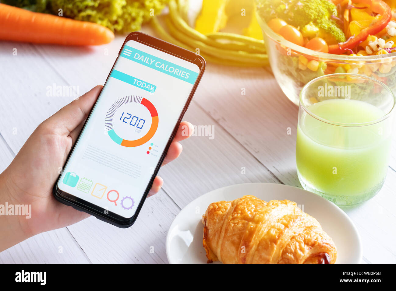 Kalorien zählen und die Lebensmittelüberwachung Konzept. Frau mit Kalorienzähler Anwendung auf Ihrem Smartphone mit Salat, Gemüse, Orangensaft und einem Croissant auf d Stockfoto