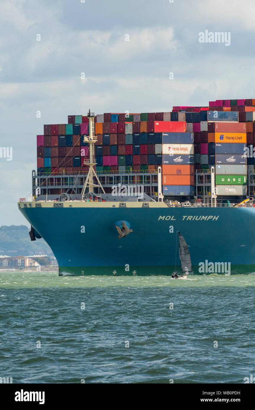 Eine kleine Yacht unter dem Bogen einer großen massiven Container-Schiff in den Solent. Stockfoto