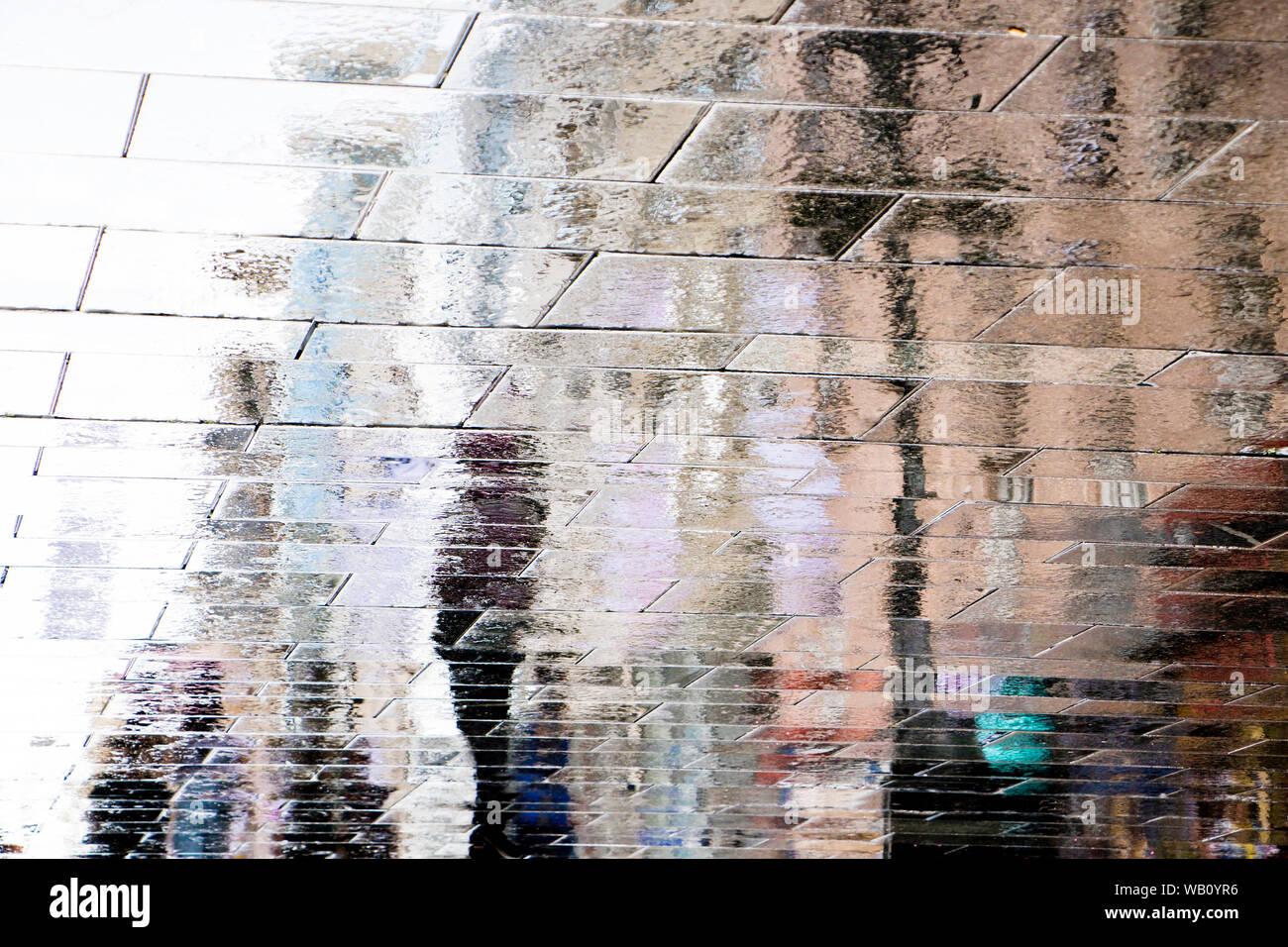 Unscharfe Reflexion Schatten Silhouetten, die laufen auf einer nassen Straße Pudel in der Stadt Fußgängerzone Stockfoto