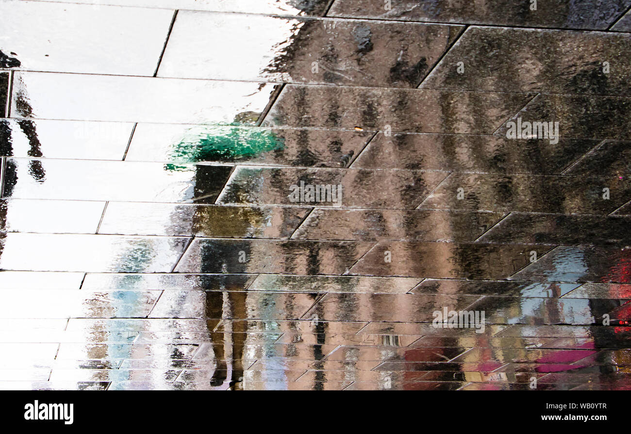 Unscharfe Reflexion Schatten Silhouette eines Mädchens zu Fuß unter dem Dach auf einer nassen Straße Pudel in der Stadt Fußgängerzone Stockfoto