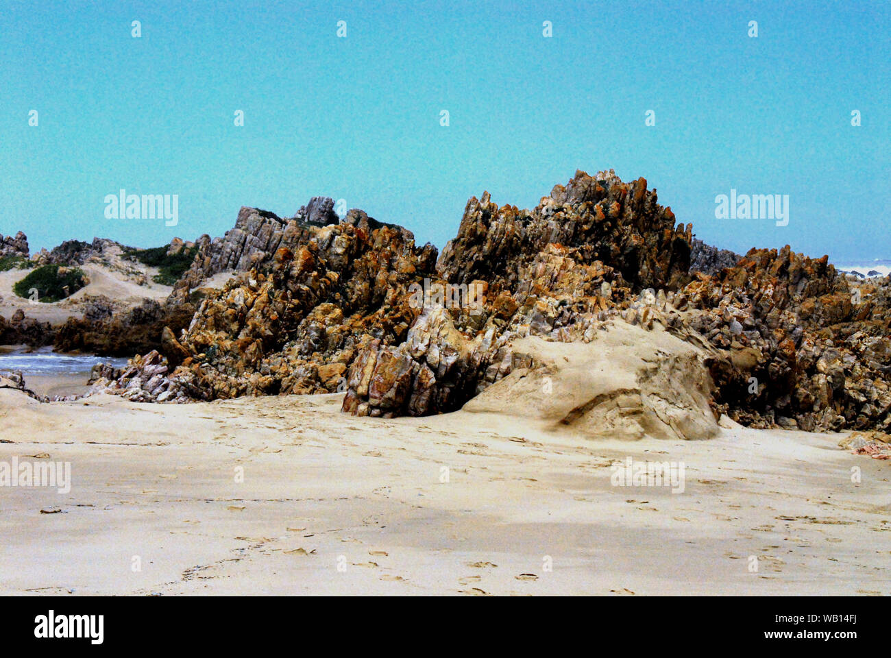 Das vulkanische Gestein bis hervorragt, am Strand in der Nähe von Knysna, Südafrika erzeugt einen schönen Hintergrund mit viel Platz für Ihre Kopie. Stockfoto