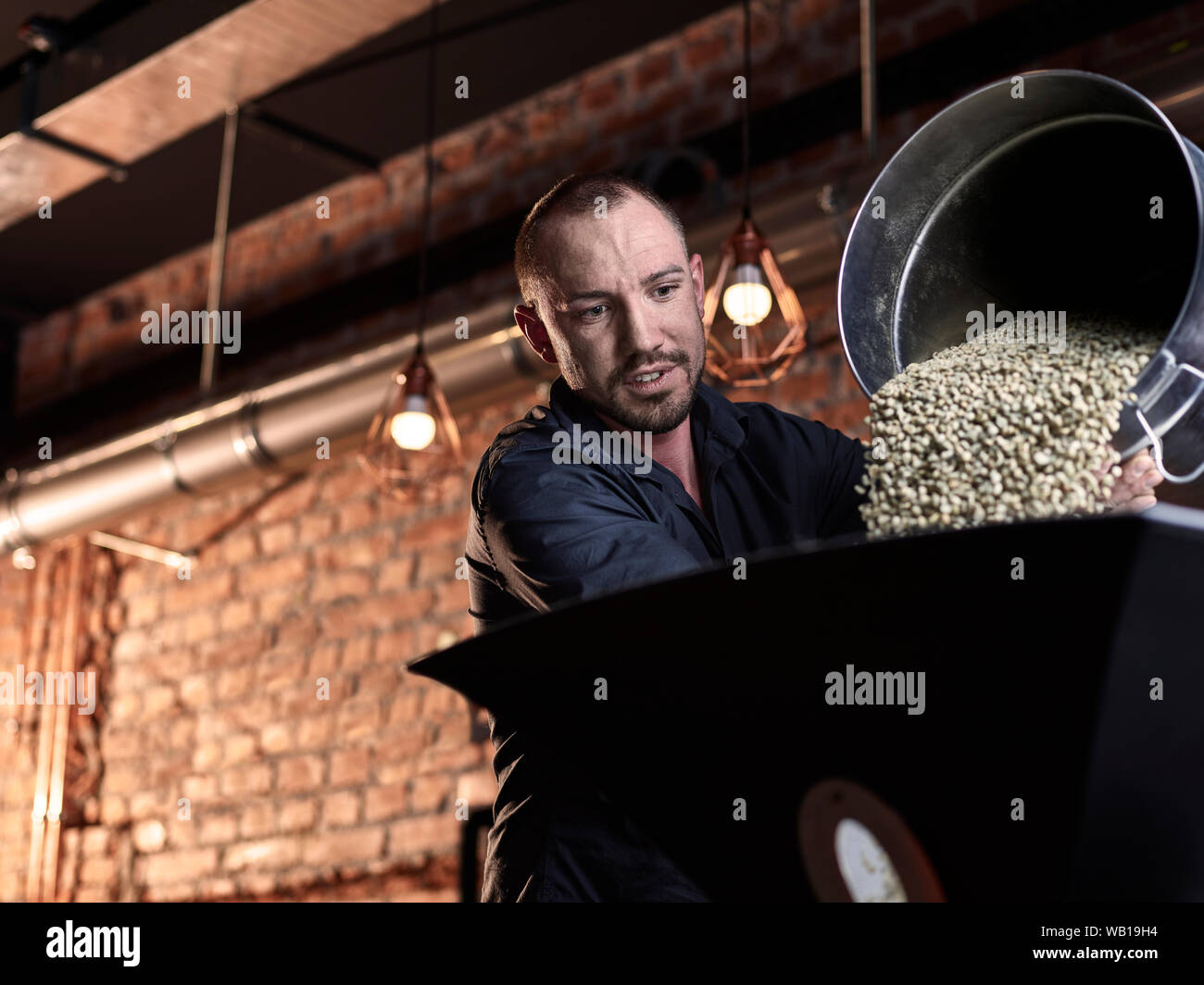 Mann gießen grüne Kaffeebohnen in Kaffeeröster Stockfoto