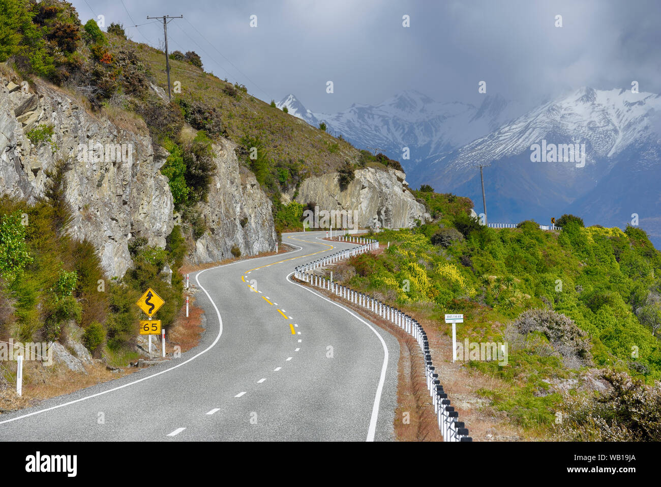 Neuseeland, Südinsel, kurvenreiche Straße in Landschaft entlang des Lake Hawea mit südlichen Alpen im Hintergrund Stockfoto
