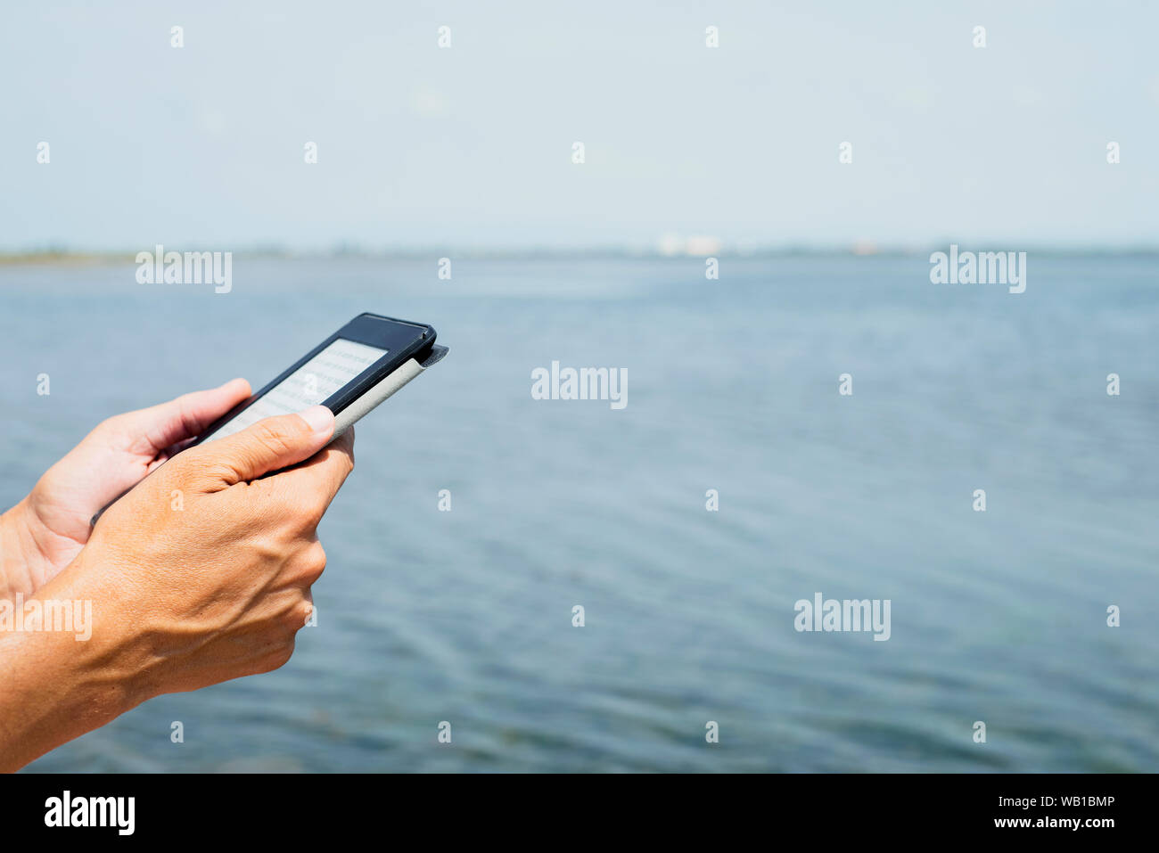 Nahaufnahme eines jungen kaukasischen Mann draußen Lesen in einer Tablette oder e-Reader neben dem Wasser Stockfoto